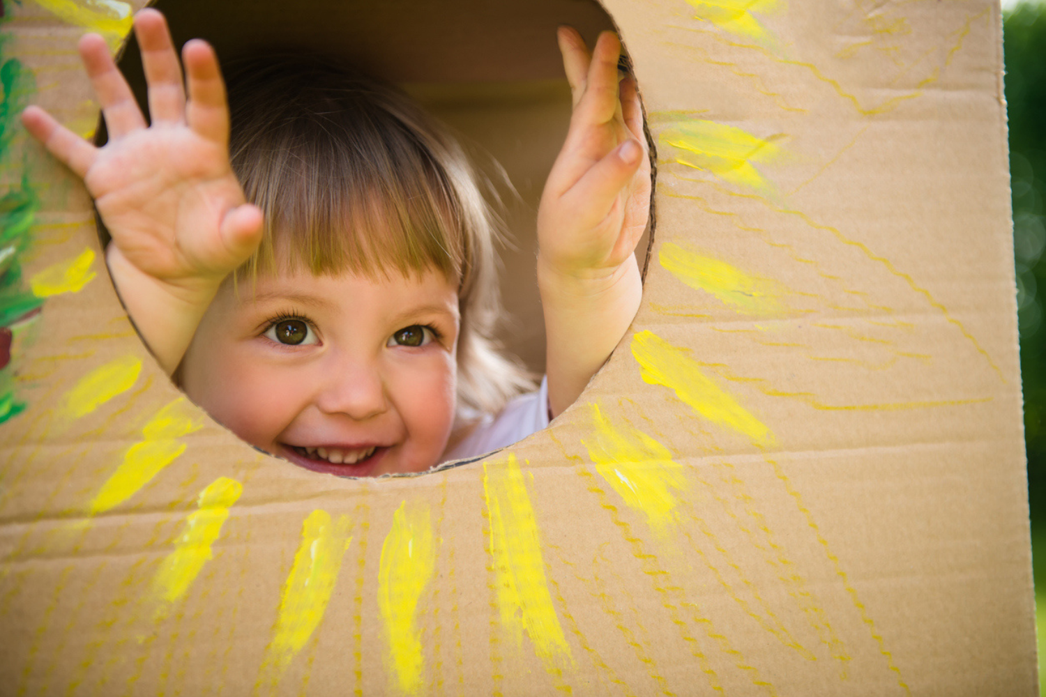 Little child looking through window of children's house made of big box